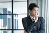 a man wearing a suit standing in front of a window thinking